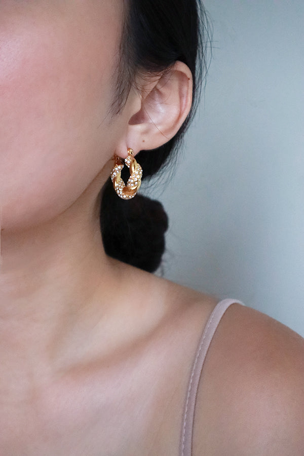 耳朵佩戴一枚奢華的金色扭紋環狀耳環,精緻鑲嵌著閃爍的鋯石。