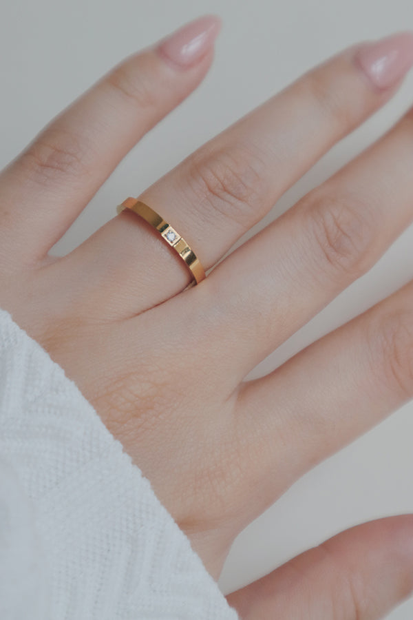 A close-up photo of a womans hand wearing a single cubic zirconia stone set in the center. Its simple yet refined design, ideal for stacking with other rings or as a standalone piece.