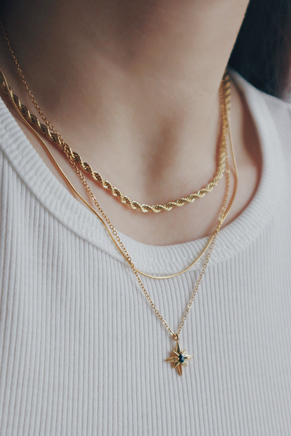 A woman wearing a set of must-have gold layering necklaces, featuring varying chain designs and a small pendant on the longest chain.