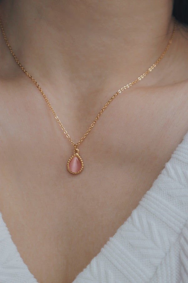 Close-up of a woman wearing a pink gemstone necklace with a teardrop-shaped pendant, paired with a white textured V-neck top, ideal for feminine styles.