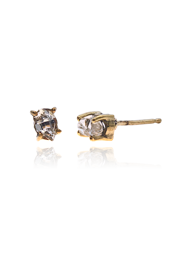 A standalone image of two pairs of gold-toned stud earrings, each featuring a rough, raw clear diamond or crystal held by prongs. The earrings are displayed horizontally on a dark background with reflections below.