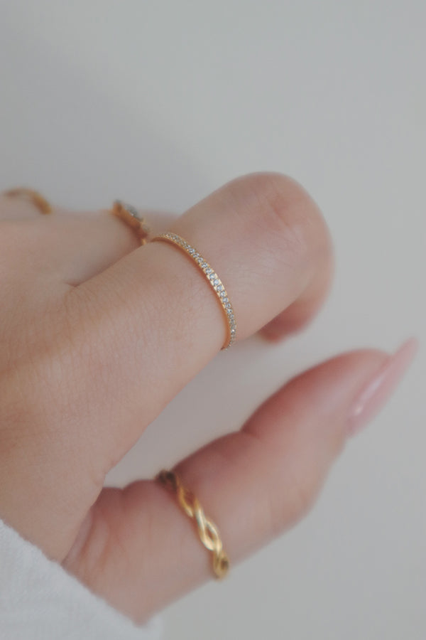 A delicate gold ring with a row of cubic zirconia stones, displayed on a clean, neutral background. The slim band and sparkling stones create a refined and elegant look, making this ring a versatile and timeless addition to any jewelry collection.