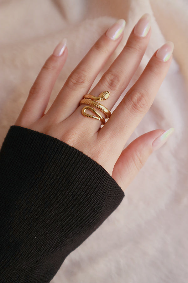 一隻手佩戴一枚設計獨特的金色盤蛇戒指,蛇身帶有紋理鱗片,頭部和尾部則光滑。