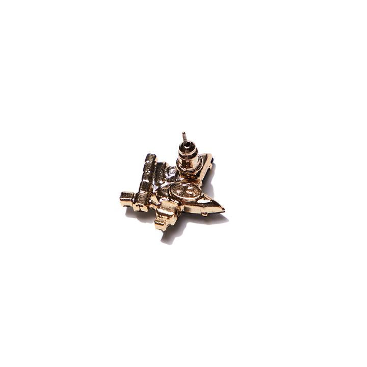 A close-up, angled shot of the back of a single gold-toned stud earring, which has an ornate, possibly star-shaped, design on its front, visible around the post. The earring casts a shadow on a white surface.