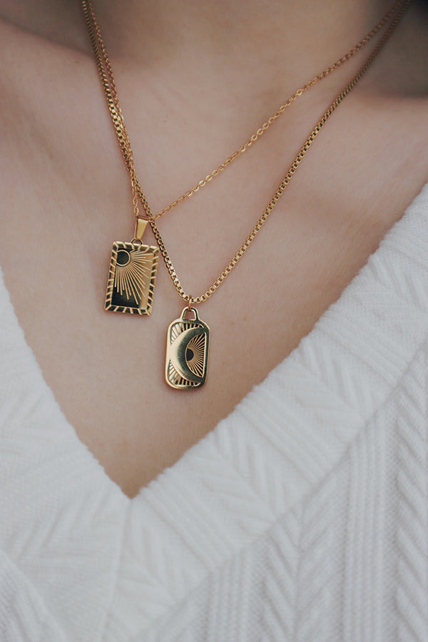 Close-up of a woman wearing a tarnish-free gold necklace featuring two layered pendants, each engraved with sun and moon designs, styled with a white textured V-neck top.