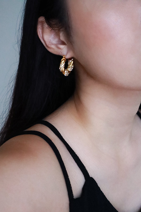 耳朵特寫,佩戴一枚潮流的鍍金扭紋環狀耳環,點綴著透明鋯石。