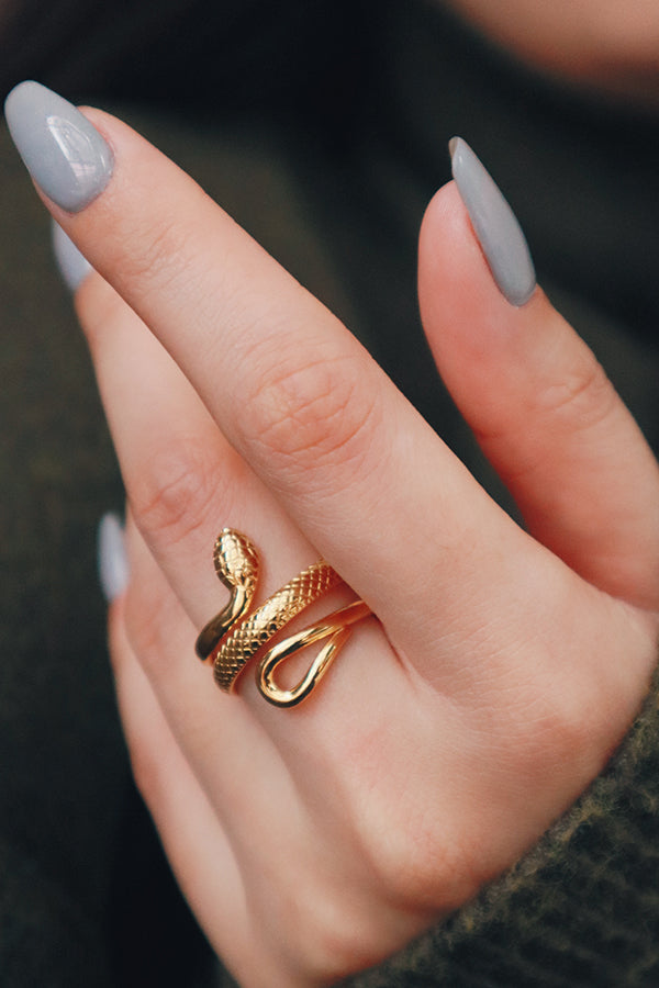 A close-up of a hand wearing a trendy gold-plated statement ring, shaped like a coiled snake with textured details on its body.