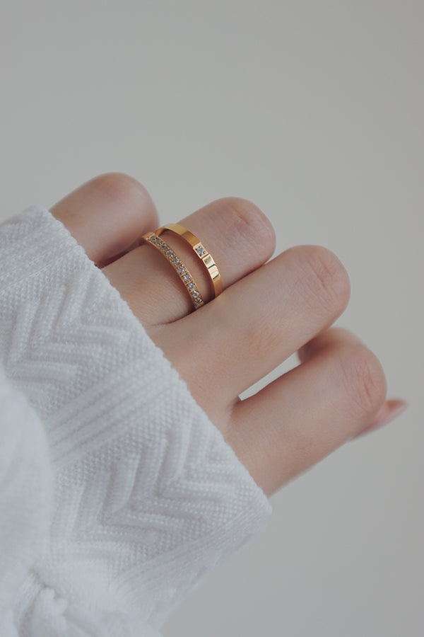 A close-up image of a womans hand wearing two trendy gold rings. One ring features a single cubic zirconia stone, while the other has multiple stones along the band, offering versatile options for stacking or wearing alone.