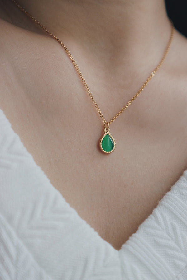 A woman wearing a trendy green gemstone necklace with a teardrop-shaped pendant, styled with a white textured V-neck top, perfect for modern outfits.