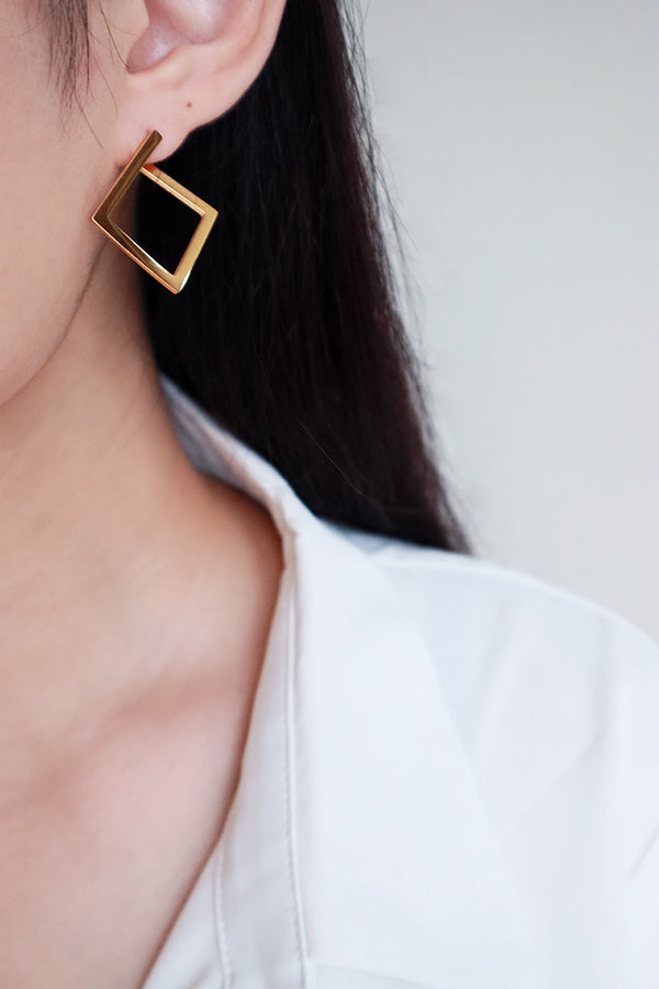 一隻耳朵佩戴著一款潮流且極簡風格的大型方形金色圓圈耳環,以其清晰的幾何輪廓營造出獨特的時尚宣言。