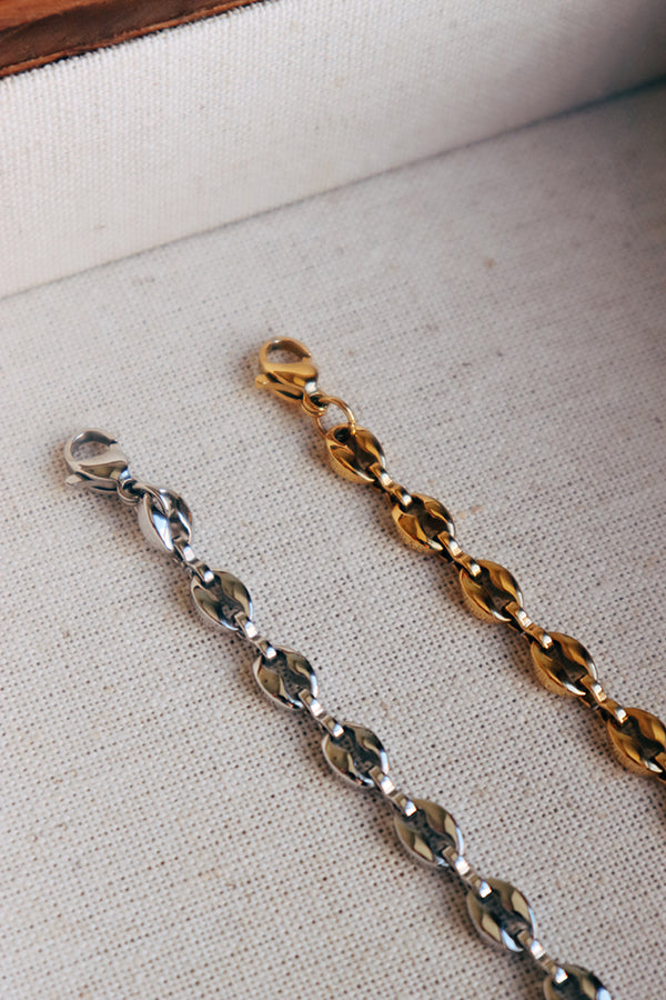 An overhead shot of two Isla Everyday Link Bracelets, one in gold-tone and one in silver-tone, showing the detailed coffee-bean links and lobster clasps. They are resting side-by-side inside a light-colored jewelry box.