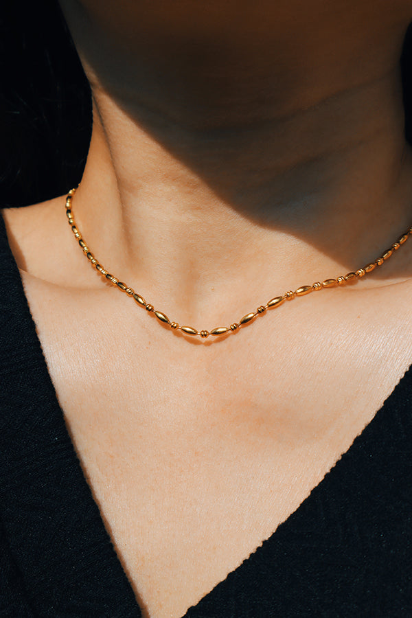 A close-up of a woman wearing an elegant gold bead necklace, perfectly complementing her black outfit.