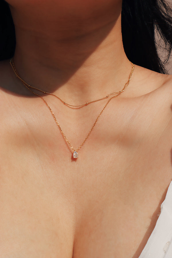 Woman in white dress layering two dainty necklaces to create a stunning style