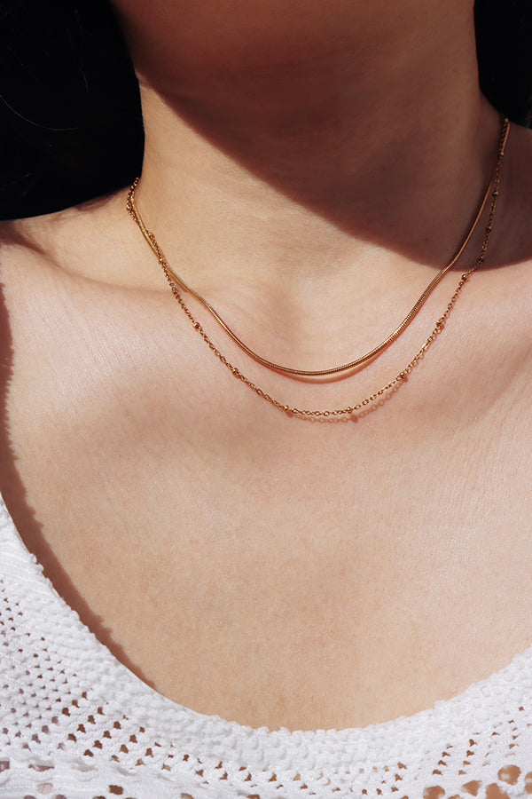 Layered gold snake chain necklace glowing in natural light, creating a refined French-inspired look.