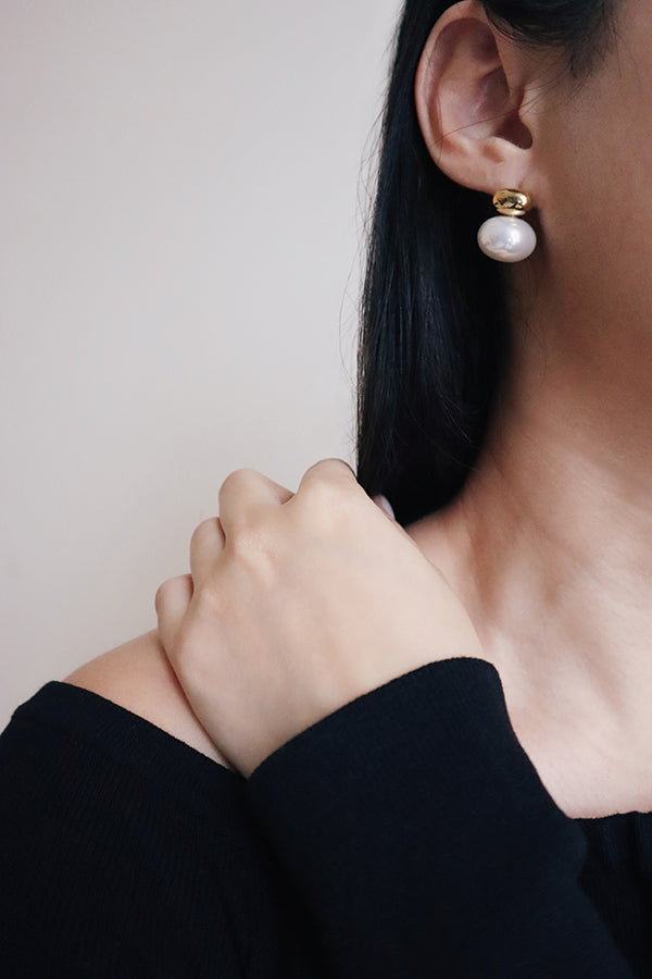 Woman in black dress paired statement pearl earrings for her night outfit.