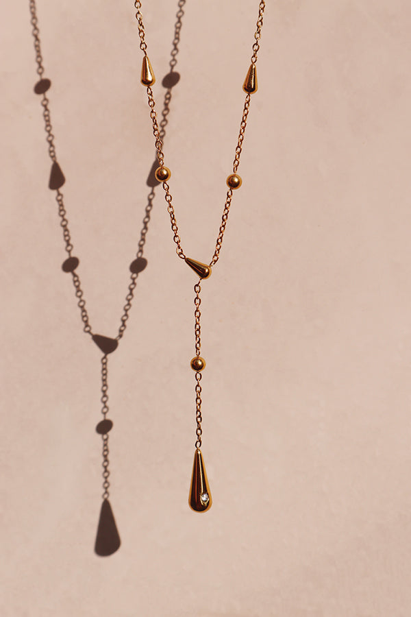 Gold beaded lariat necklace with a slim teardrop pendant displayed flat, perfect for solo wear or layering.