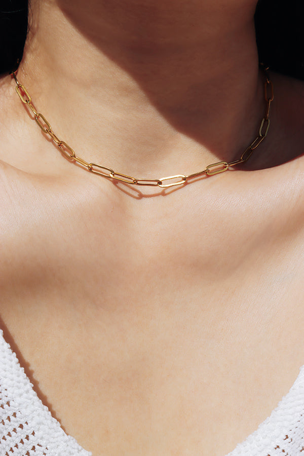 Gold chain necklace close-up along the collarbone, adding a warm and elegant glow.
