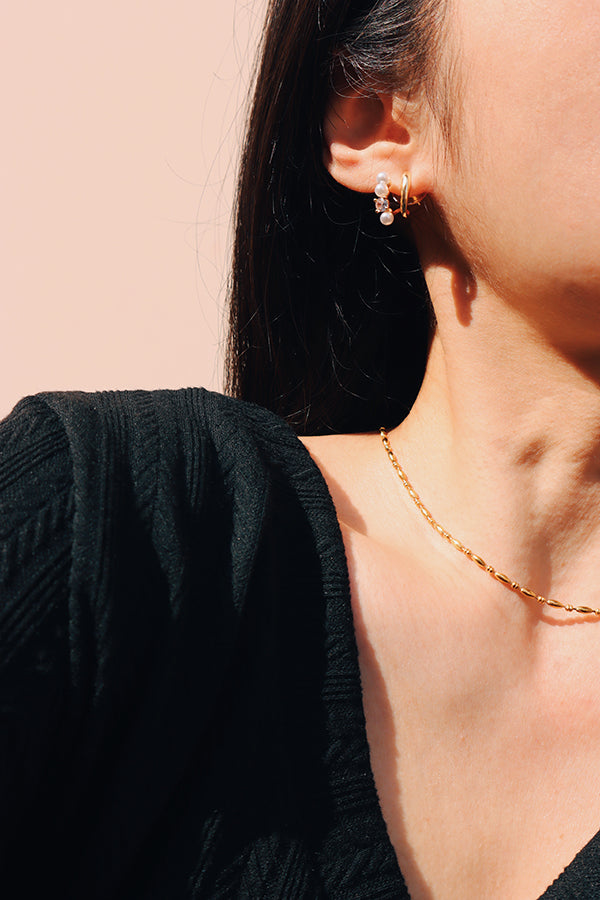 A stylish woman wearing gold and pearl stud earrings, perfect for an elegant and modern jewelry statement.