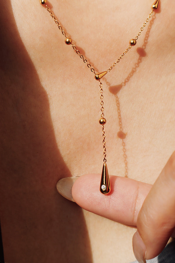 Close-up of a gold teardrop pendant accented with a small sparkling zircon stone for subtle shine.
