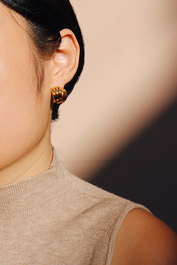 A close-up view of a woman wearing layered gold stud earrings, with soft shadows adding depth to the elegant, vintage-inspired design.