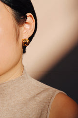A close-up view of a woman wearing layered gold stud earrings, with soft shadows adding depth to the elegant, vintage-inspired design.