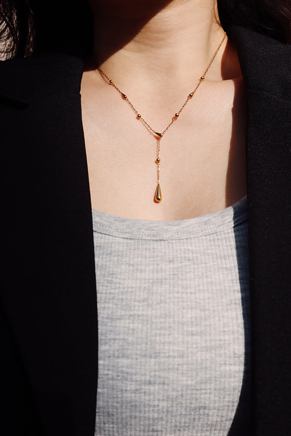 Minimalist gold Y necklace styled with a grey top and blazer, creating a refined French-inspired look.