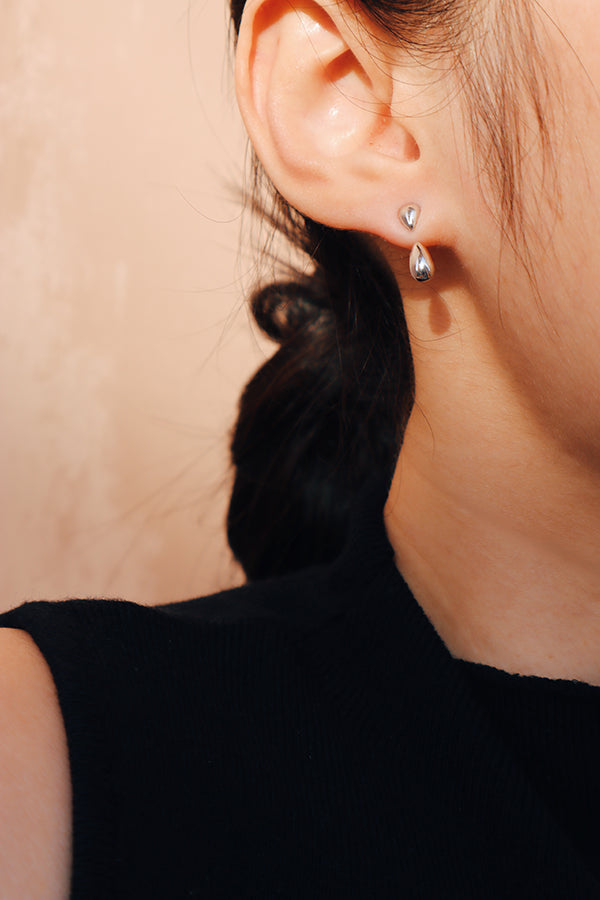 Close-up of sleek silver teardrop earrings styled on woman's earlobe with low bun hairstyle