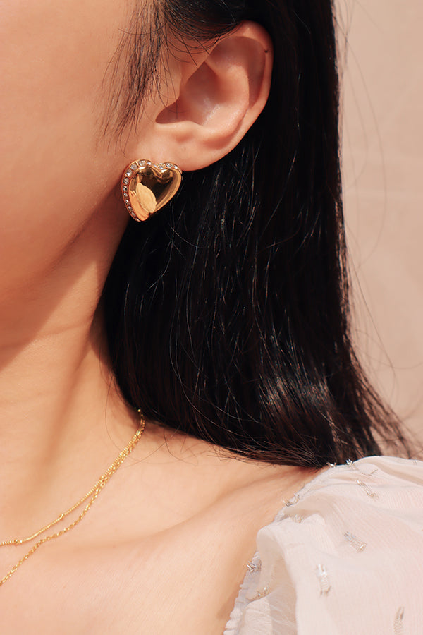 Gilr wearing white top and a gold heart shaped earring under the sun