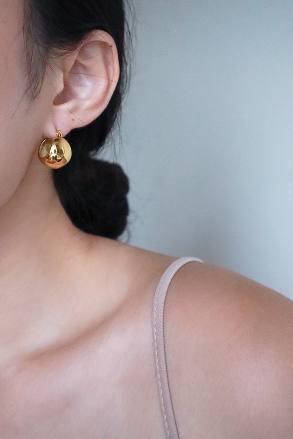 A girl wearing gold plated globe earrings shows her half face to the camera