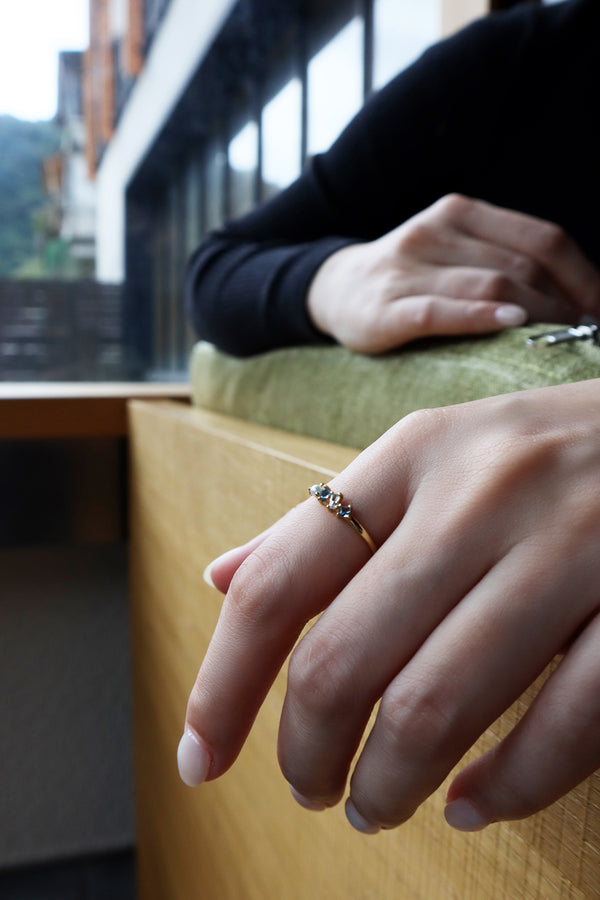 Model in black sweater wearing slim gold ring sitting on sofa showing half her body