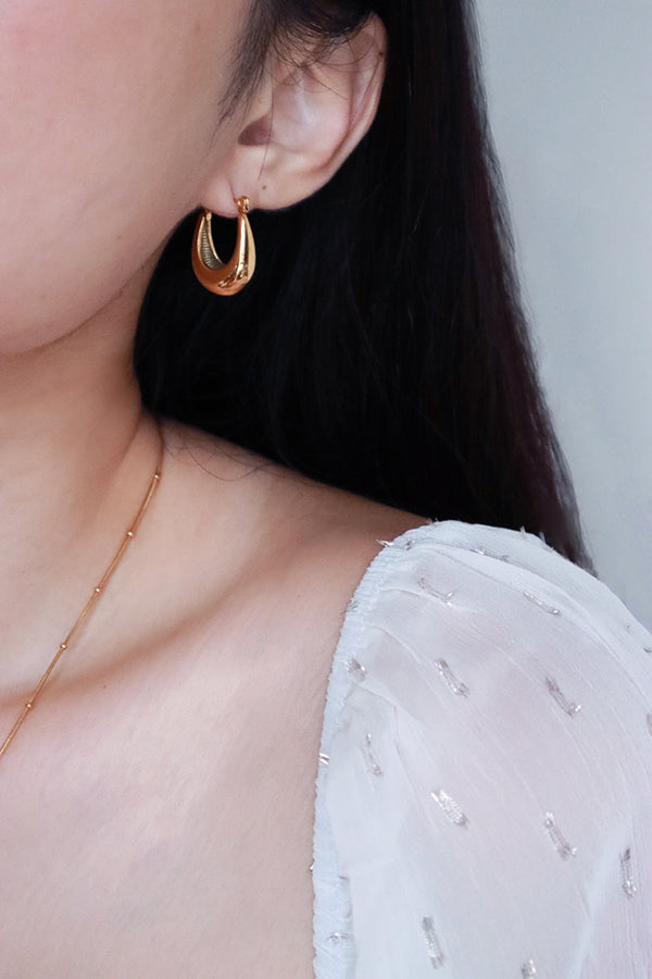 Girl in white shirt showing her half face that wearing trendy gold hoop earrings