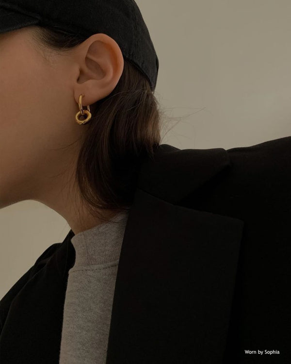 Earring model with gold hoop earrings wearing a black coat and hat