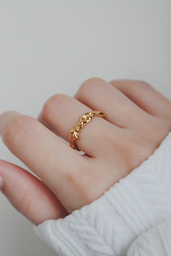 A close-up photo of a womans hand featuring a gold ring with an irregular, abstract design. The ring's uneven surface and artistic shape create a fashionable and unique look, perfect for complementing various outfits.