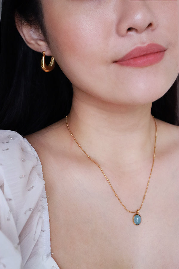 Black hair woman in white dress wearing gold earrings and gemstone necklace