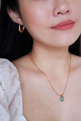 Black hair woman in white dress wearing gold earrings and gemstone necklace