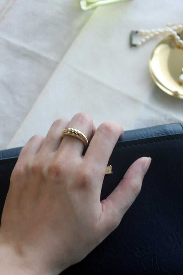 Gold ring with red color on the inside on middle finger holding a handbag by SH & Co.