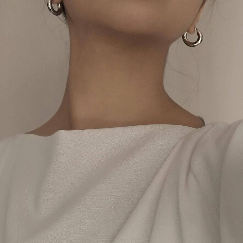 White dressed girl wearing a pair of silver hoop earrings showing bottom half of her face 