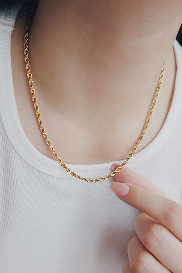 Close-up of a trendy gold rope chain necklace being adjusted by a woman, showcasing its intricate weave and glossy finish.